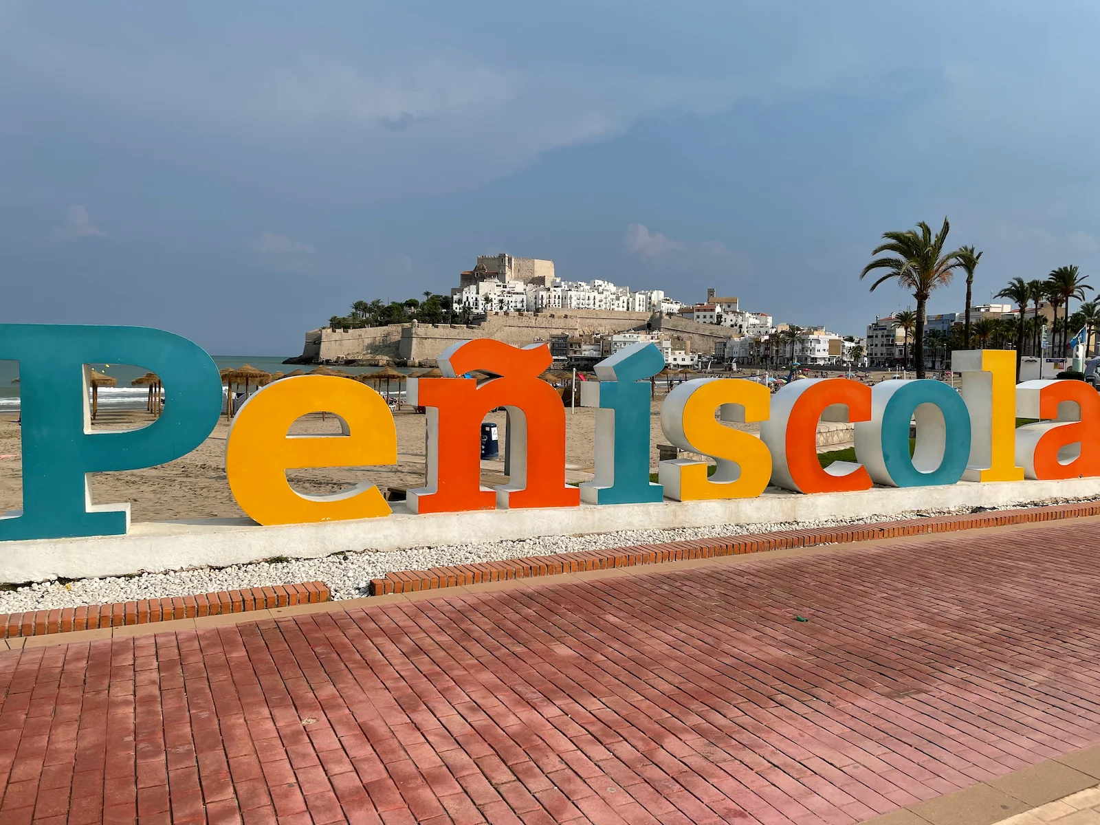 Letrero colorido de Peñíscola con el castillo al fondo y la playa bañada por el sol
