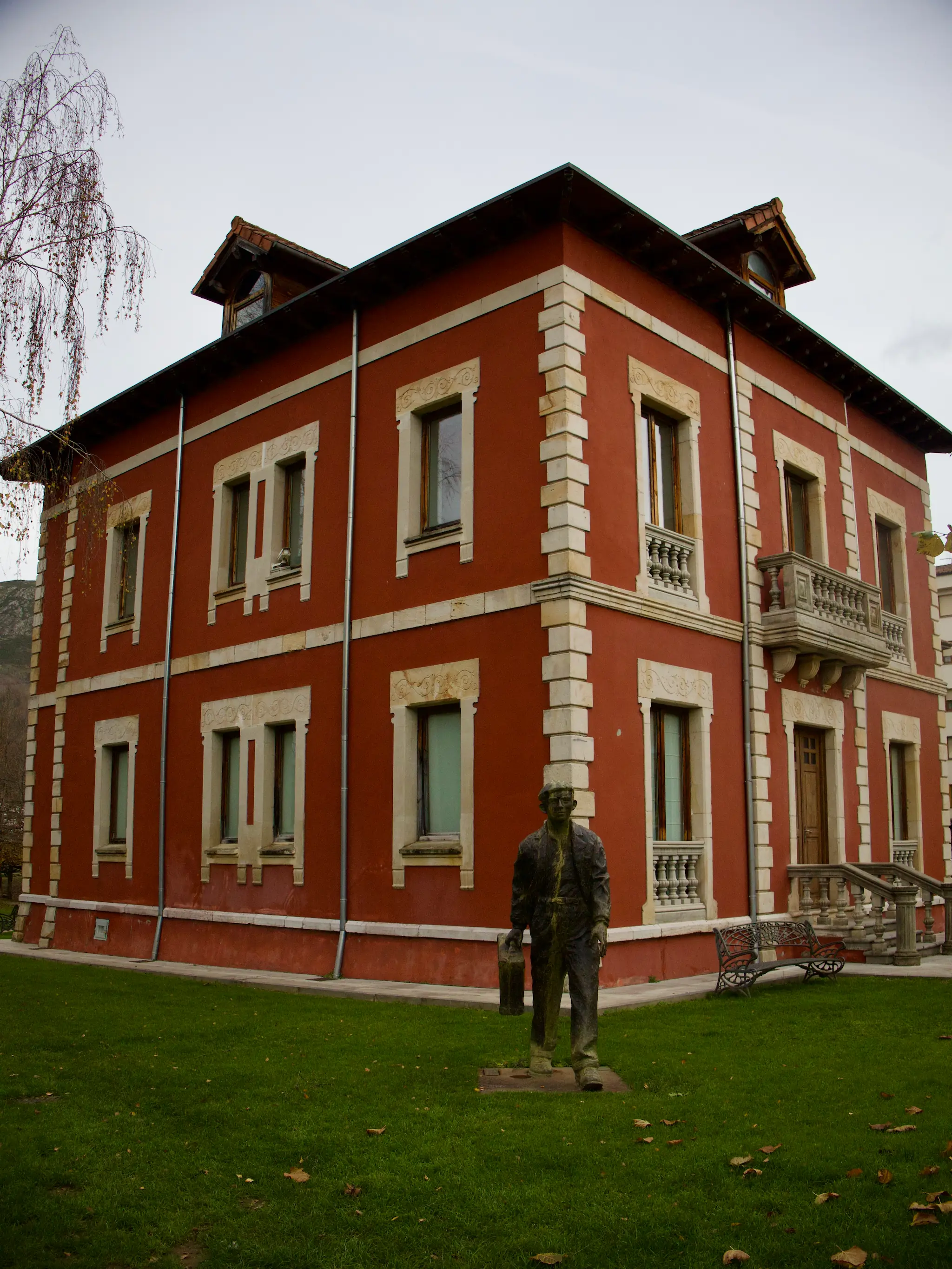 Casa señorial roja con balcones de piedra y estatua en el jardín en Cangas de Onís Asturias