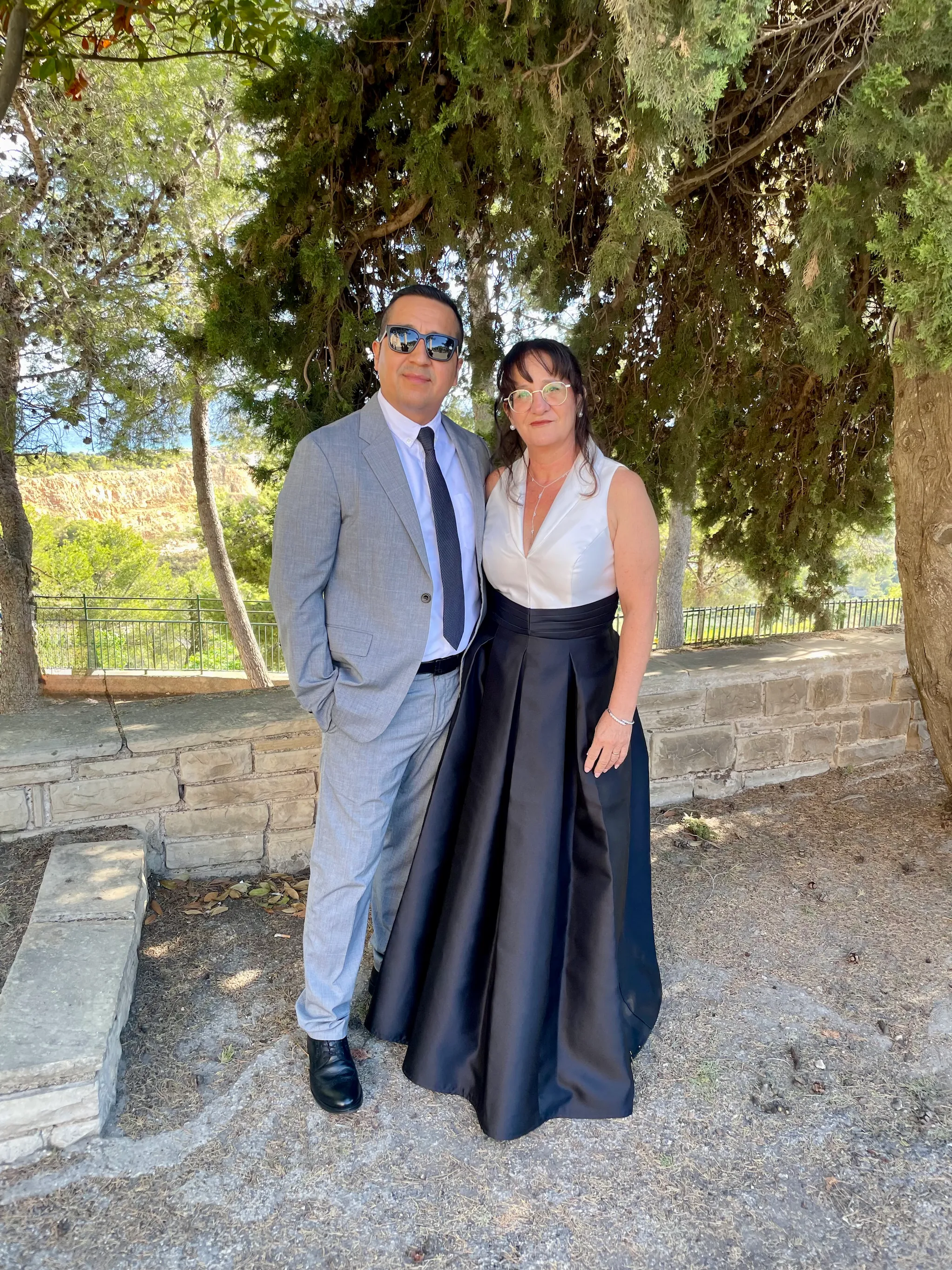 Pareja vestida de ceremonia bajo los árboles, antes de asistir a una celebración familiar.
