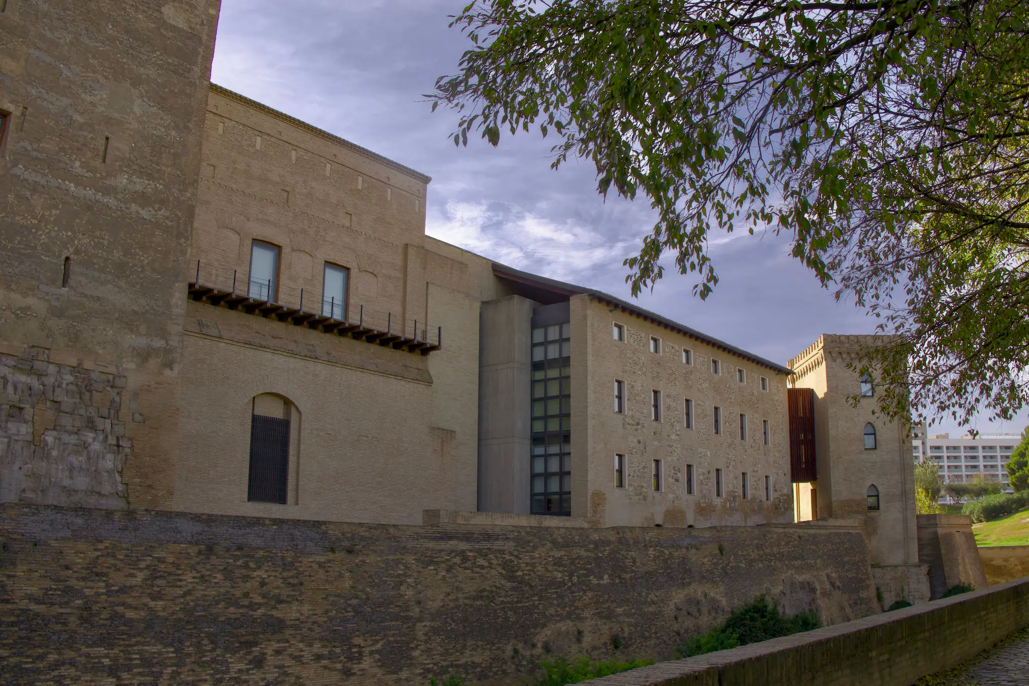 Ángulo inferior del palacio mezclando arquitectura histórica con detalles modernos bajo las ramas de un árbol
