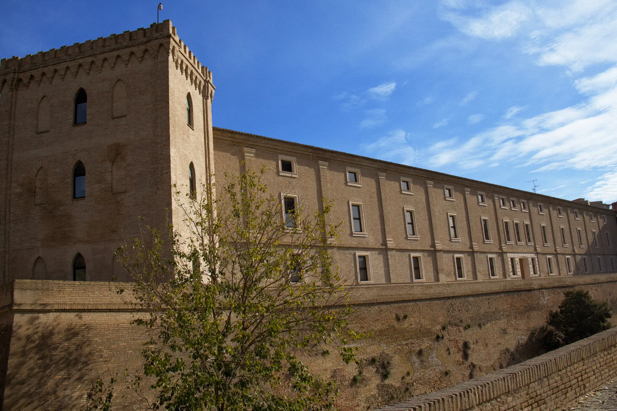 Fachada lateral del palacio con ventanas simétricas bajo un cielo azul con nubes alargadas